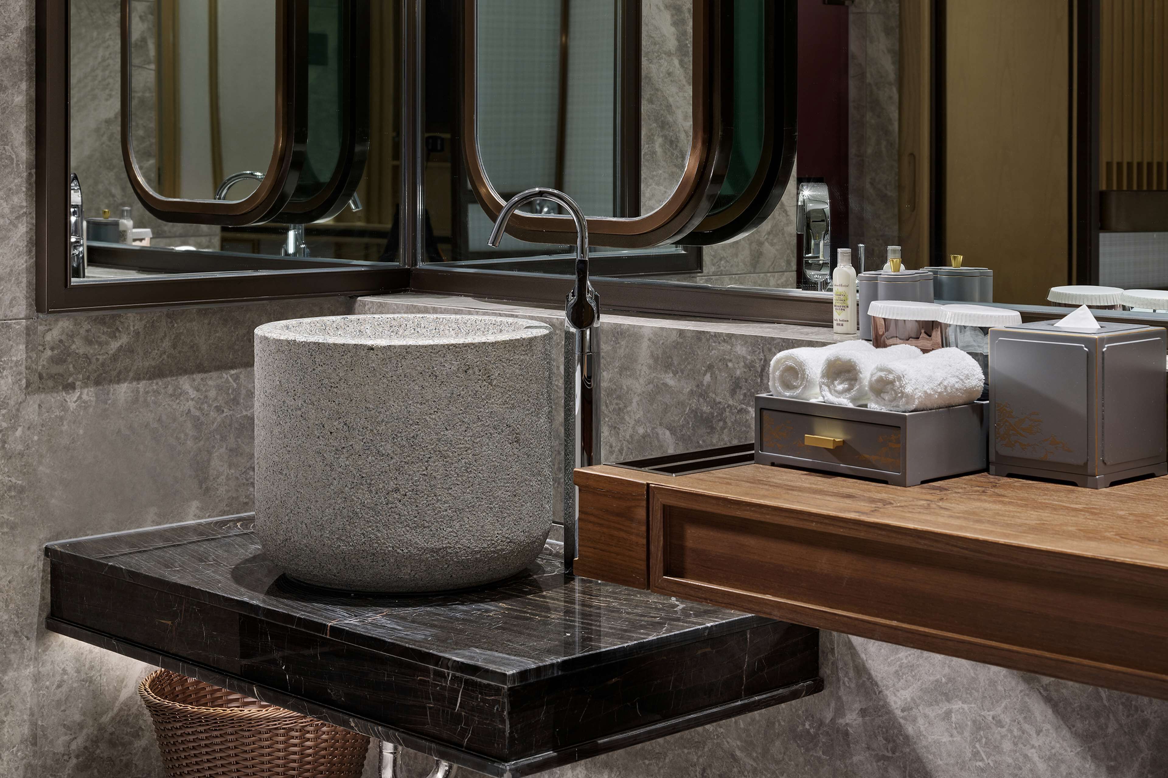 Un baño con lavamanos de granito, tocador de madera y un espejo grande.