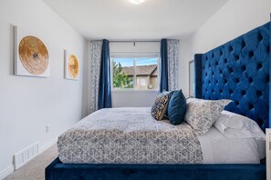 A bedroom with a large bed, a window with curtains, and two wall art pieces. - Evergreen Calgary Townhome — 3BR, Sleeps 6, Gas Fireplace, Free Parking (Calgary)