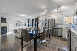 A modern kitchen with stainless steel appliances, a dining area with a glass table, and a fireplace. - Modern House with Private Backyard and Fireplace (Calgary)