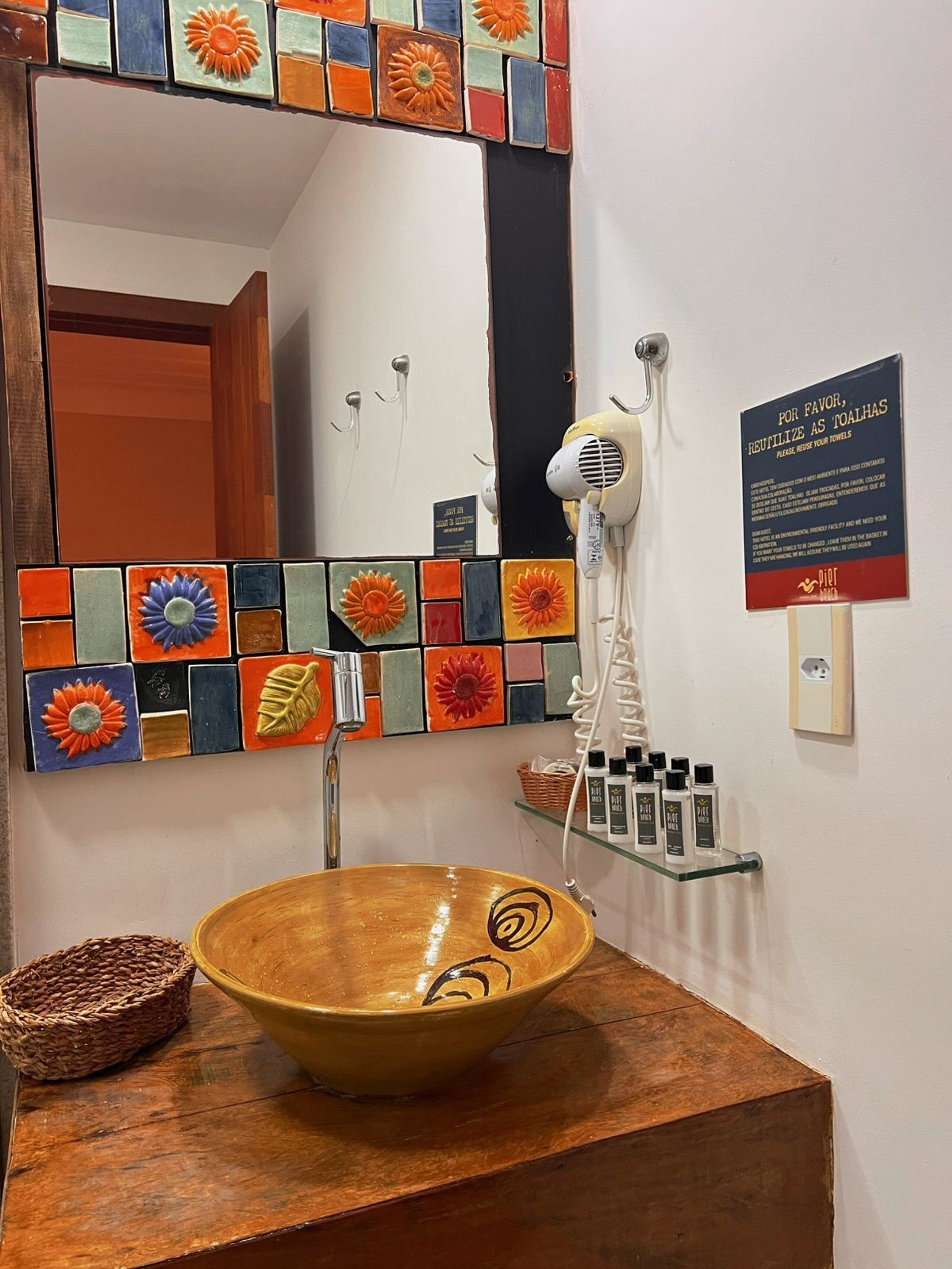 A bathroom with a wooden vanity, a bowl sink, a hairdryer, and a sign requesting towel reuse.