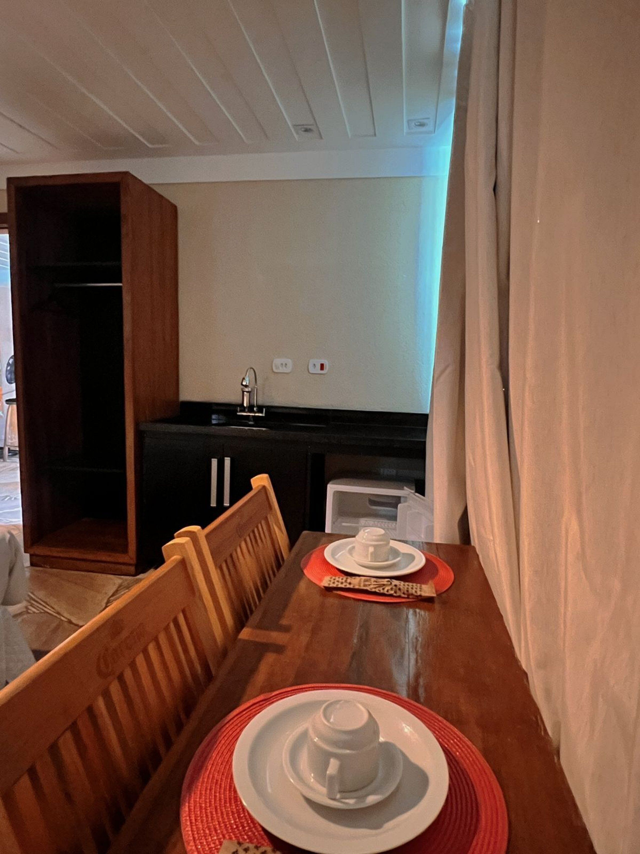 Ein Essbereich mit einem Holztisch, gedeckt für zwei Personen, einer Küche im Hintergrund und einem Schrank links.