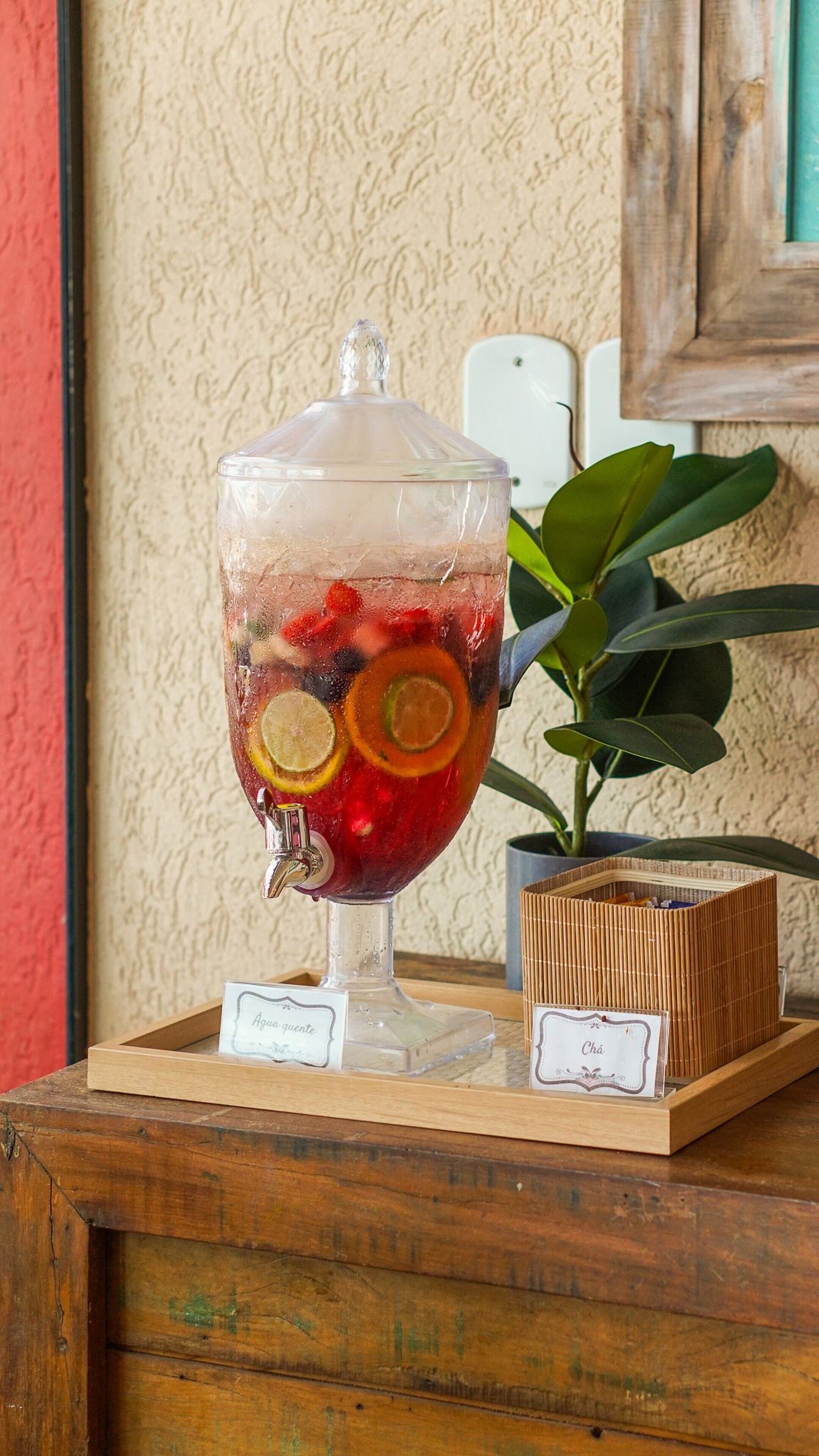 Een glazen punchkom gevuld met fruit en ijs, geplaatst op een houten tafel met een plant ernaast.
