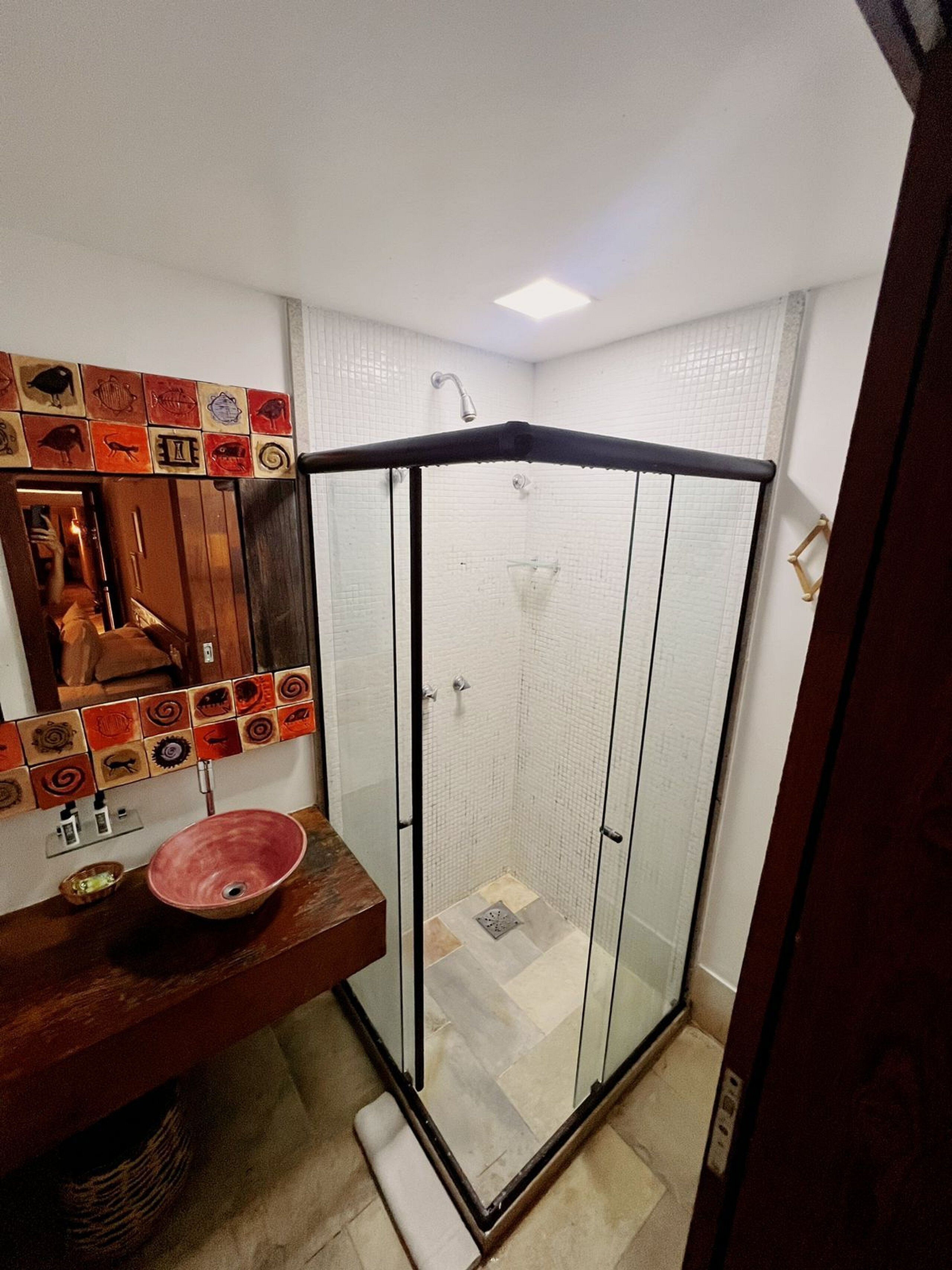 A bathroom with a glass-enclosed shower, a wooden vanity with a pink basin, and a tiled wall with animal illustrations.