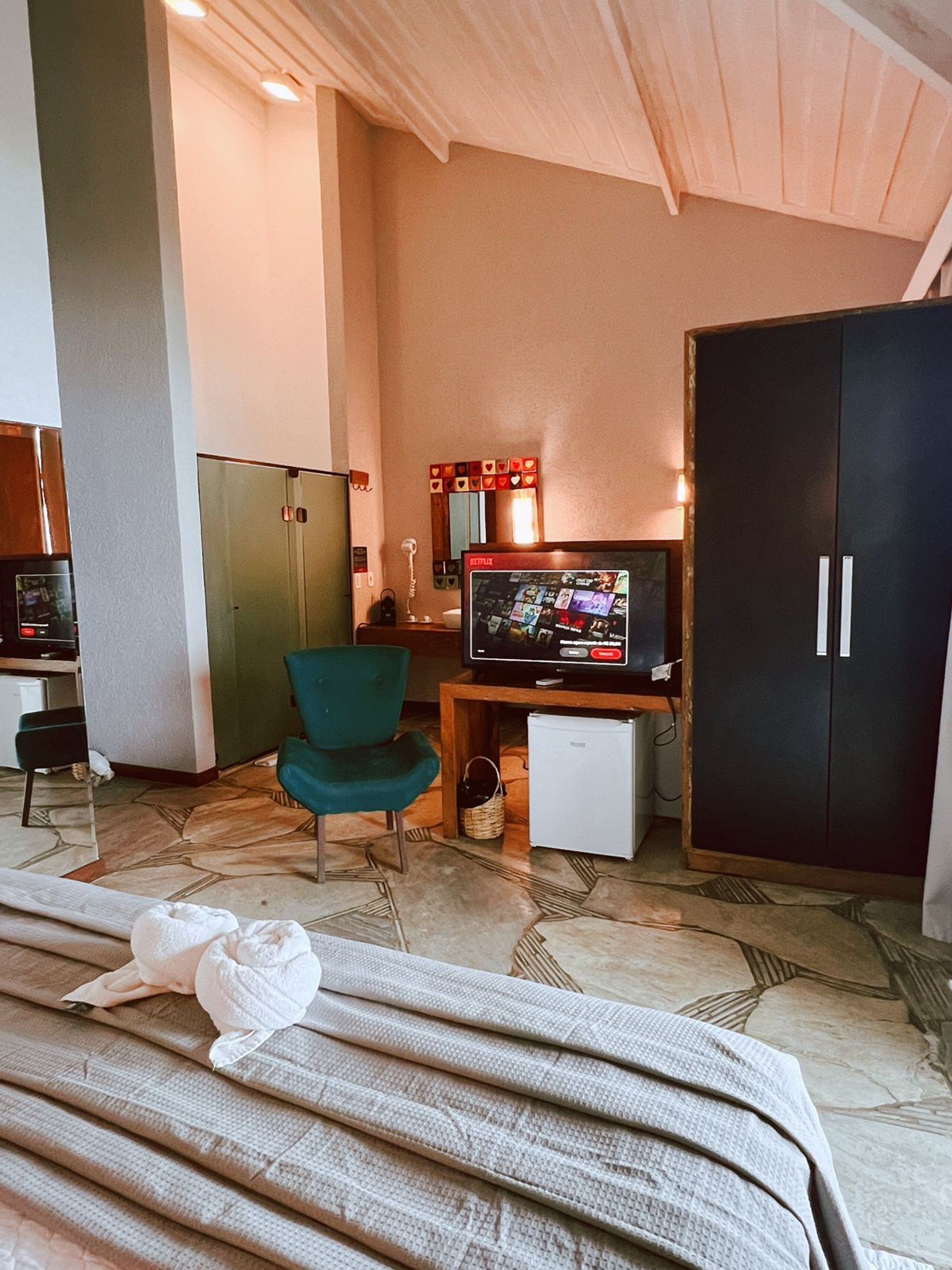 A hotel room with a television, a green chair, a wardrobe, and a small refrigerator.