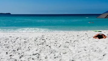 Na praia, areia branca, guarda-sóis, toalhas de praia