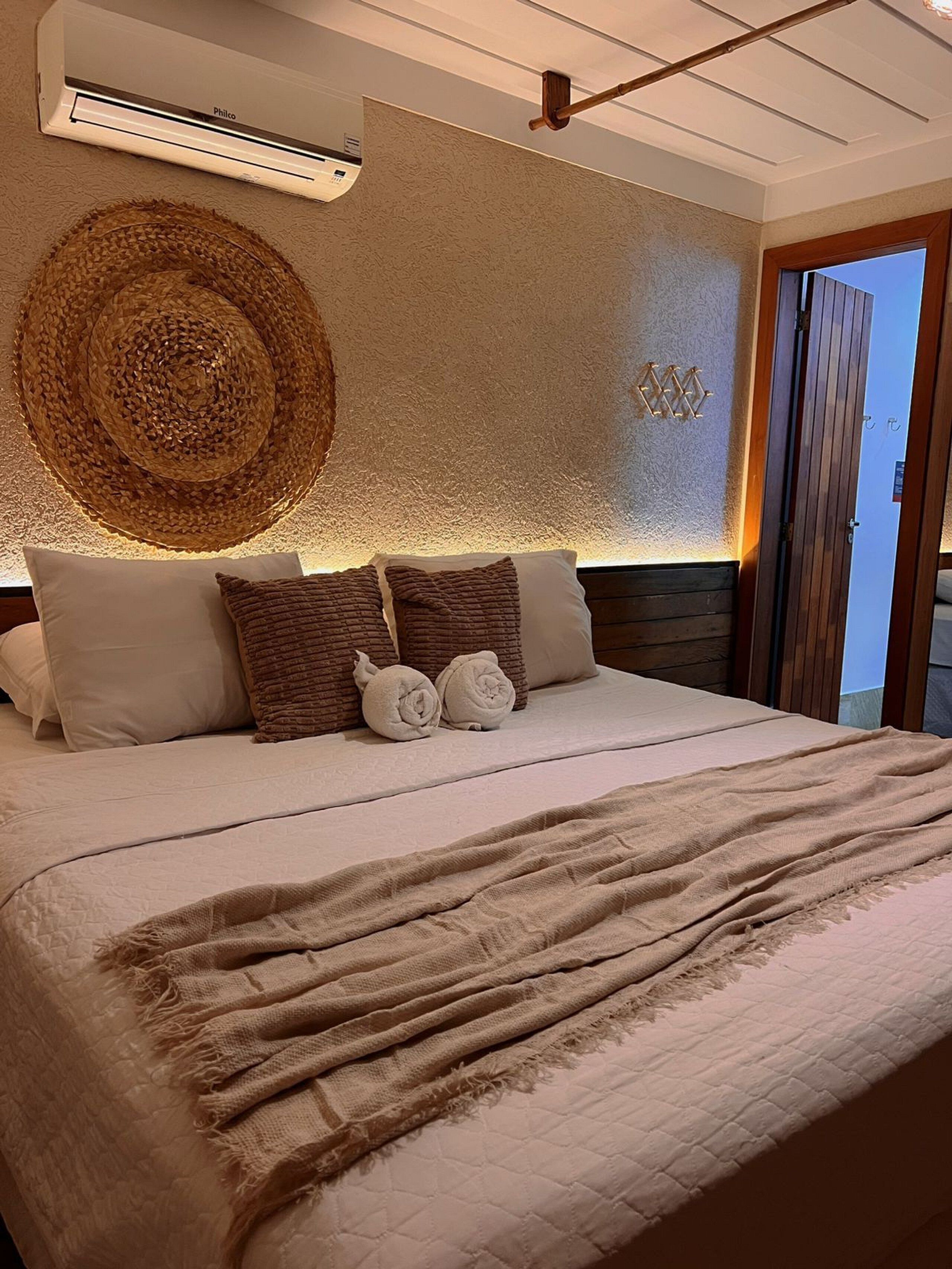Cama bem arrumada com um edredom bege e um cobertor marrom.