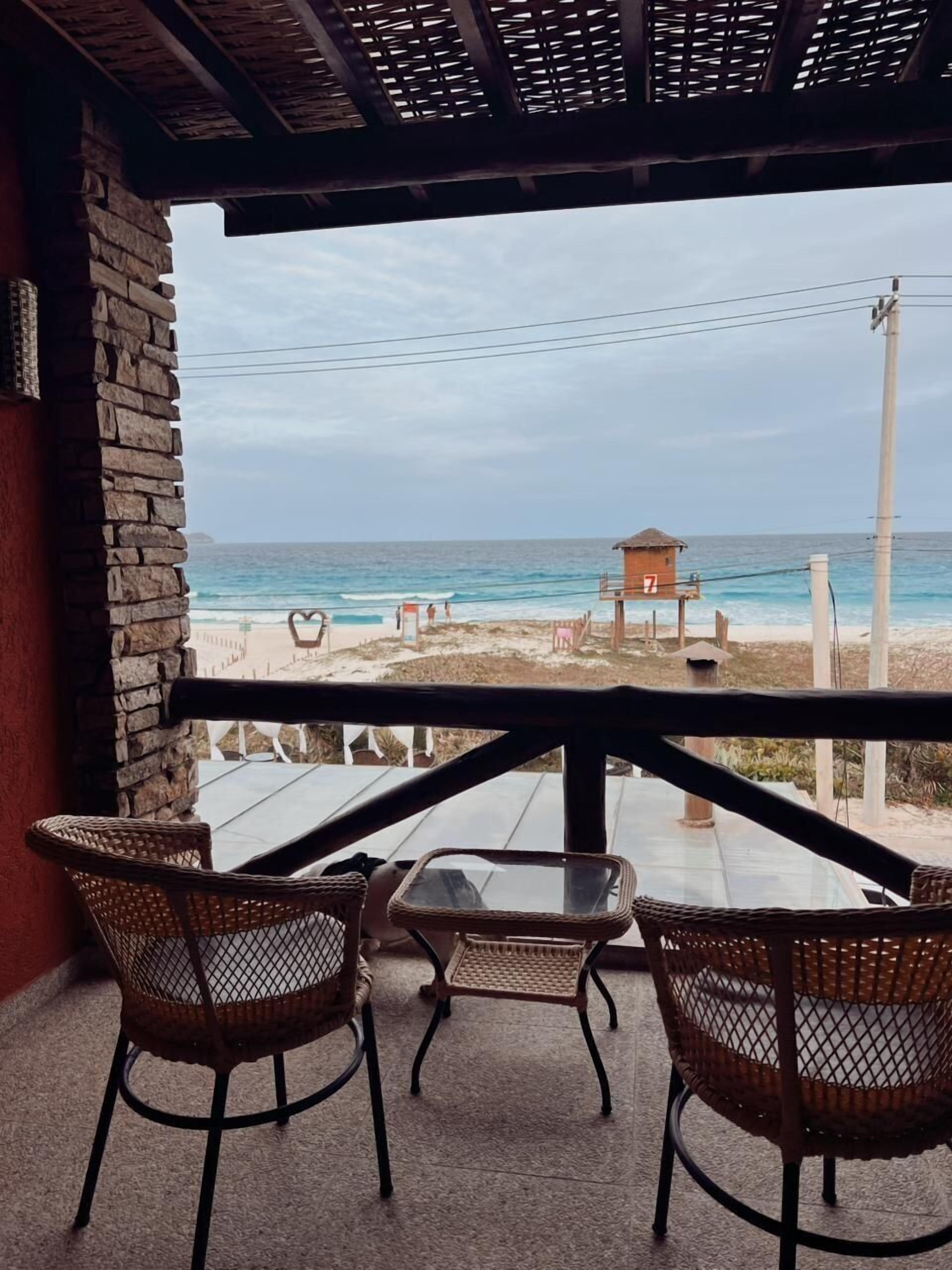 Una terraza con sillas de mimbre y una mesa, con vistas a una playa y una estructura de paja.