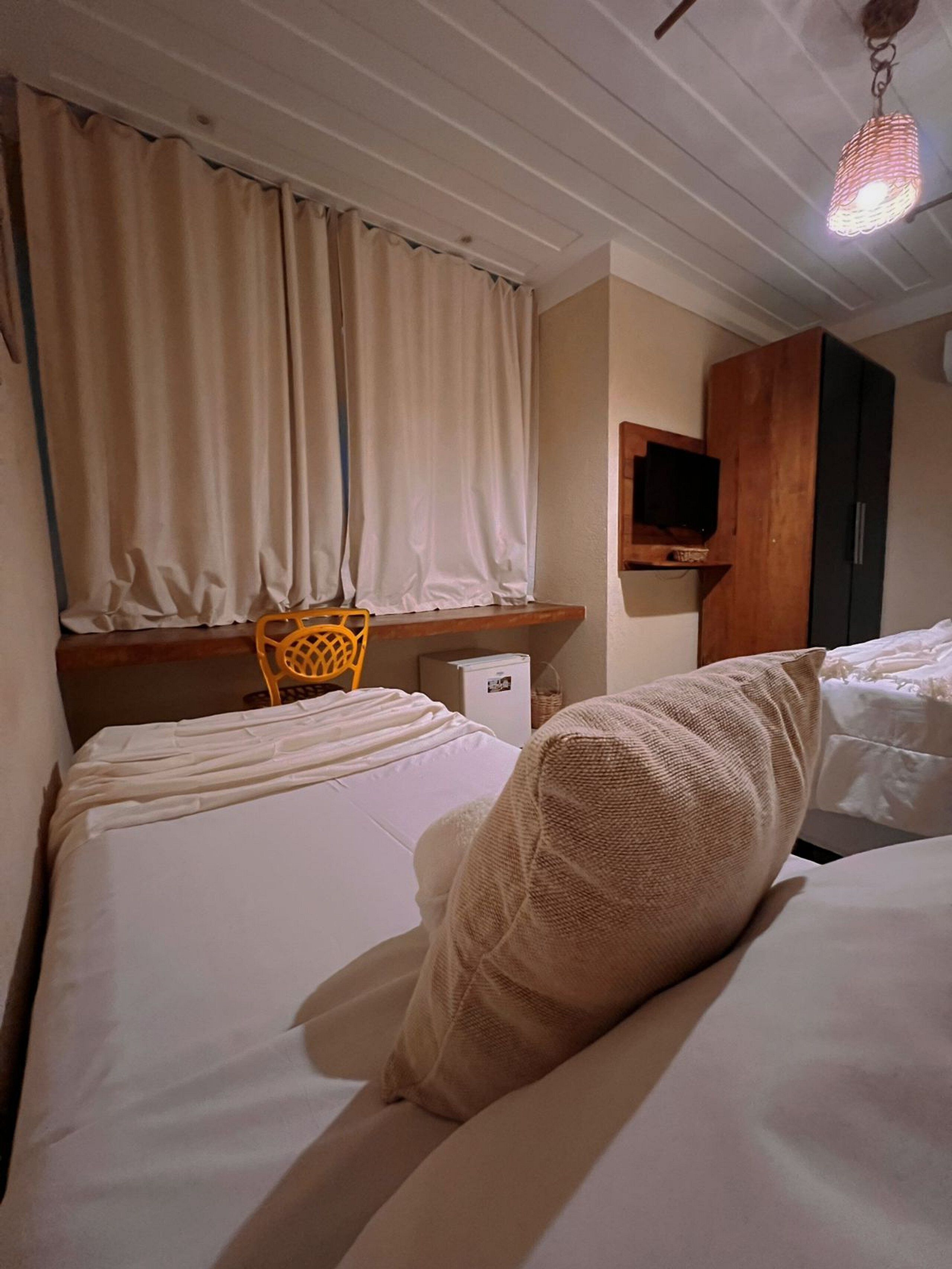 A hotel room with two beds, a wooden headboard, a television mounted on the wall, and a small table with a chair.