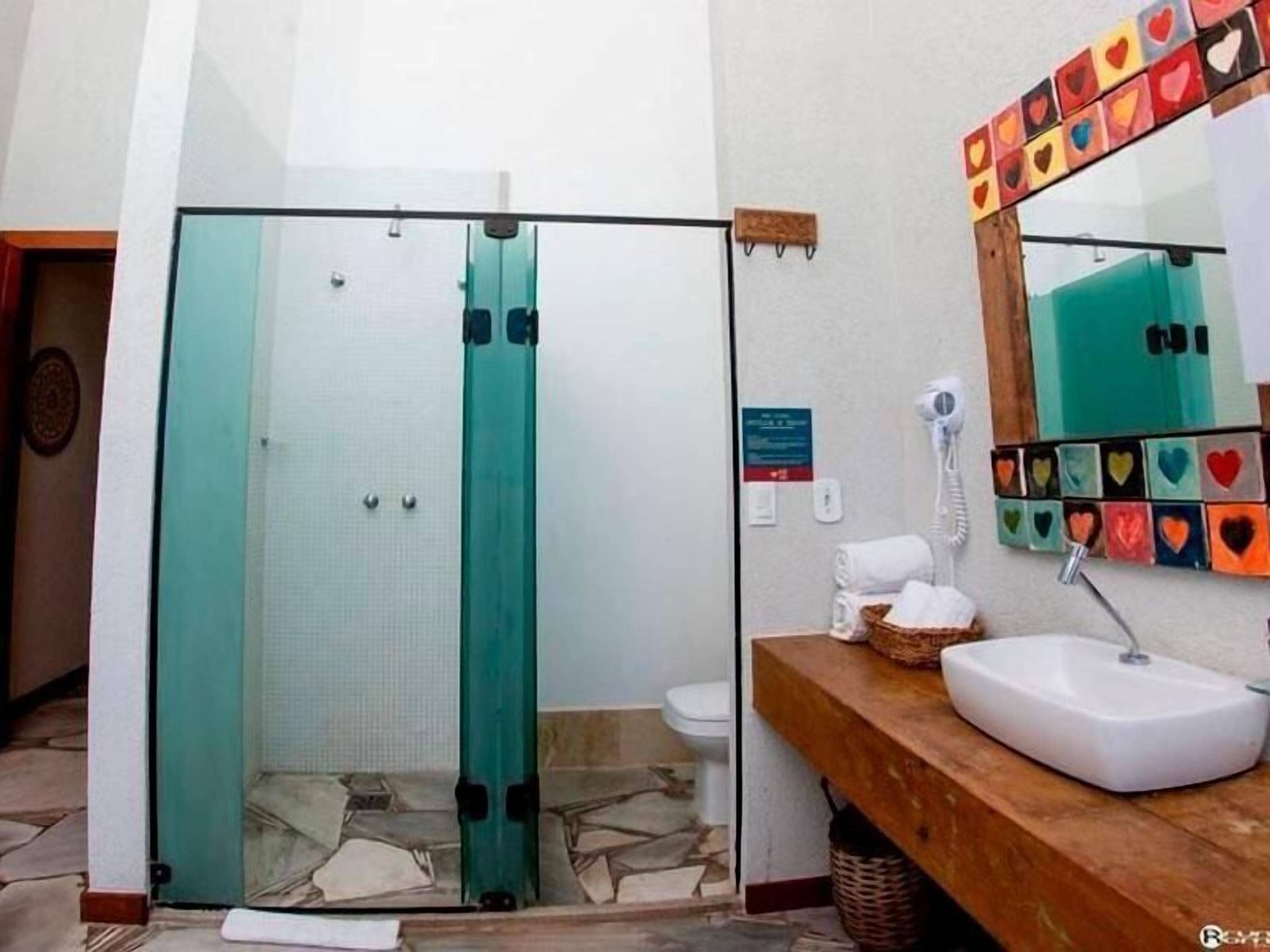 Une salle de bain dotée d’une douche à parois de verre, d’un meuble-lavabo en bois et d’un miroir orné de motifs en forme de cœur.