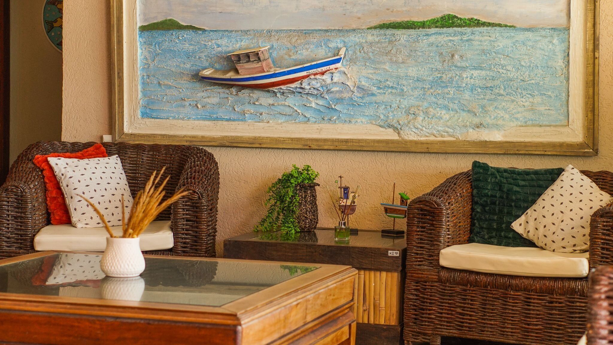 A cozy living room with wicker furniture, a glass coffee table, and a painting of a boat on water.