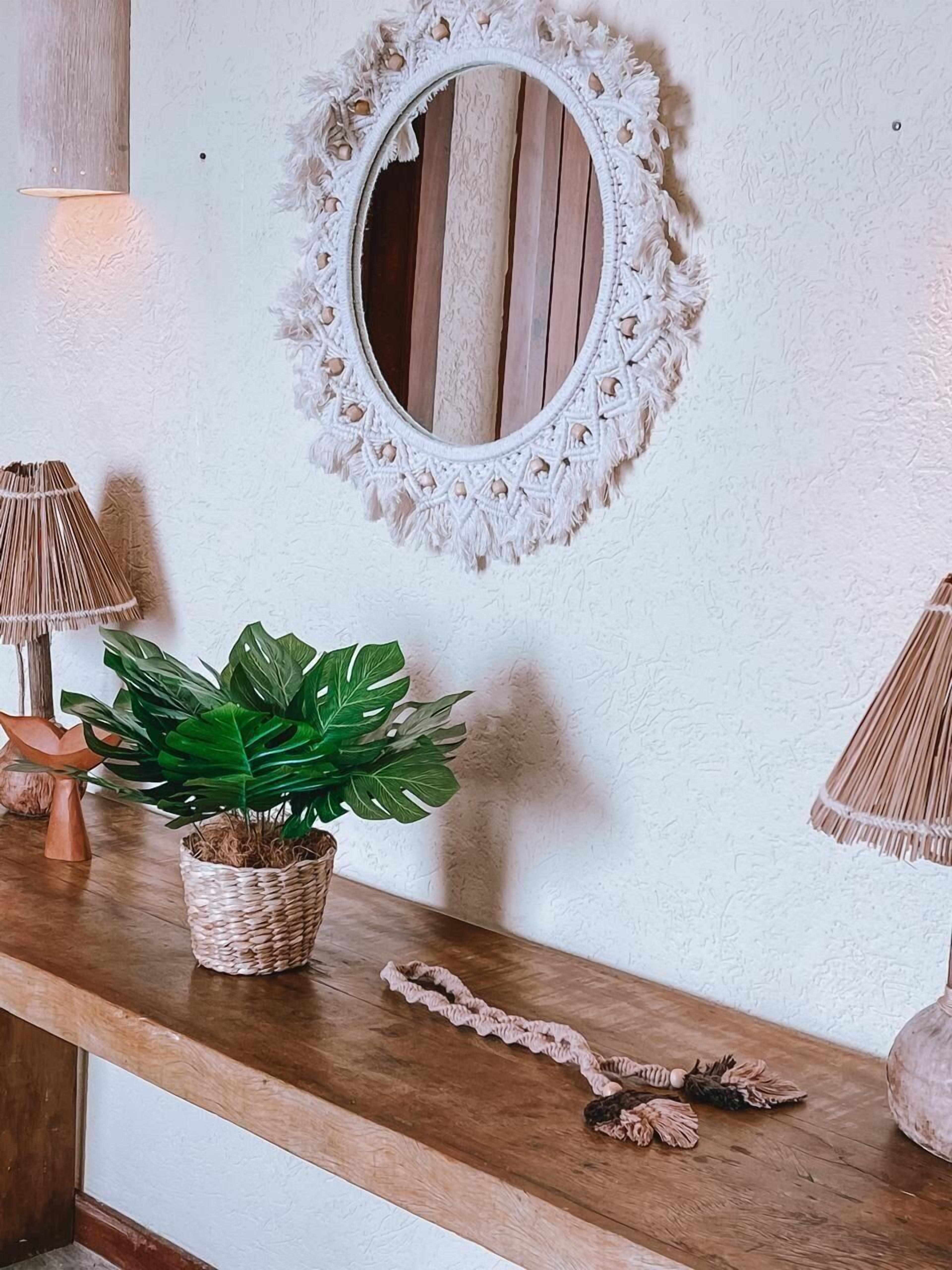 A wooden console table with a woven basket holding a green plant, a macrame mirror, and a ruffled rope.