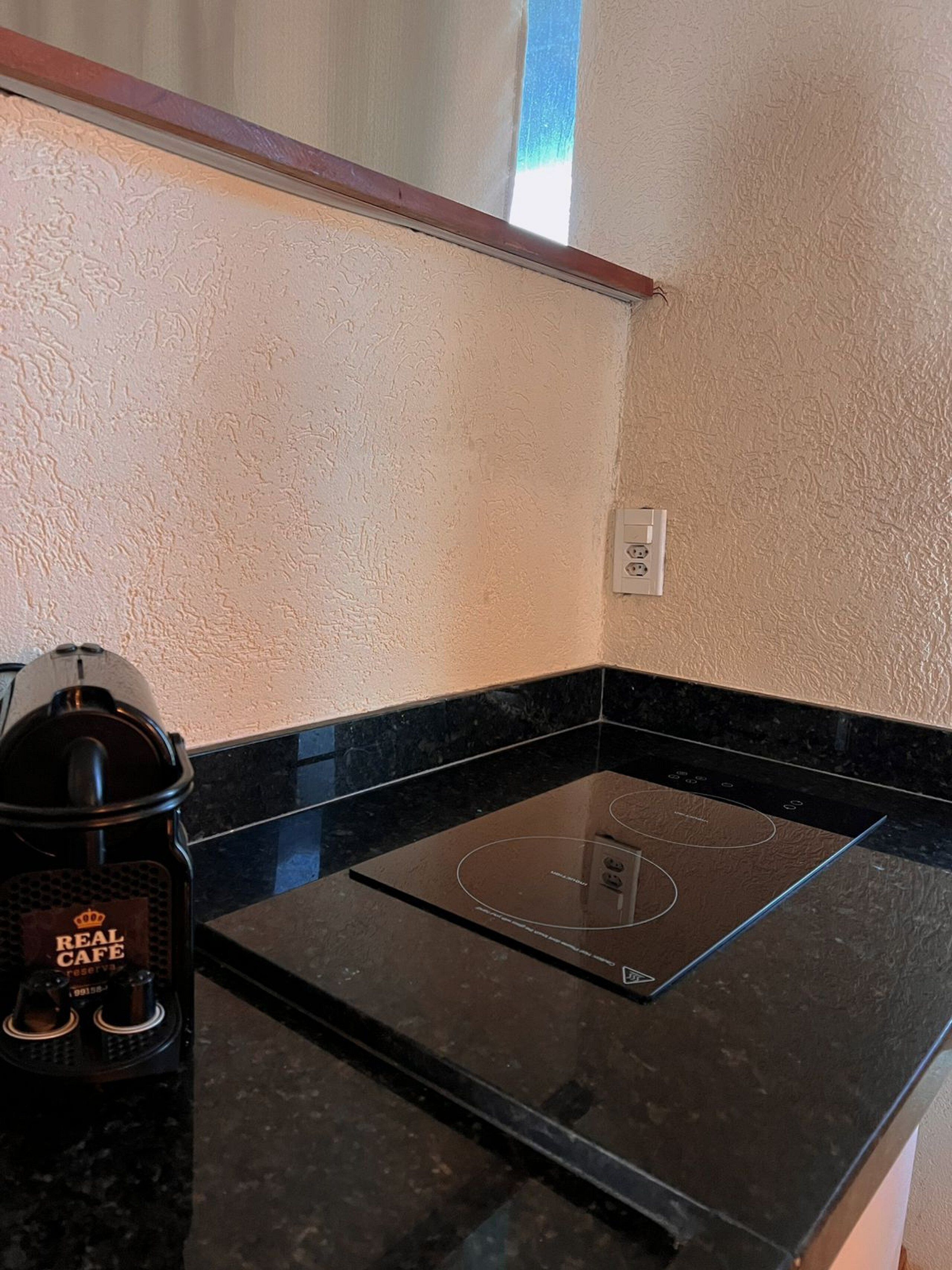 A kitchen with a black countertop, a built-in induction cooktop, and a coffee maker labeled "REAL CAFÉ RESERVA".