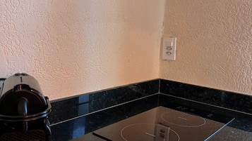 A kitchen with a black countertop, a built-in induction cooktop, and a coffee maker labeled "REAL CAFÉ RESERVA".