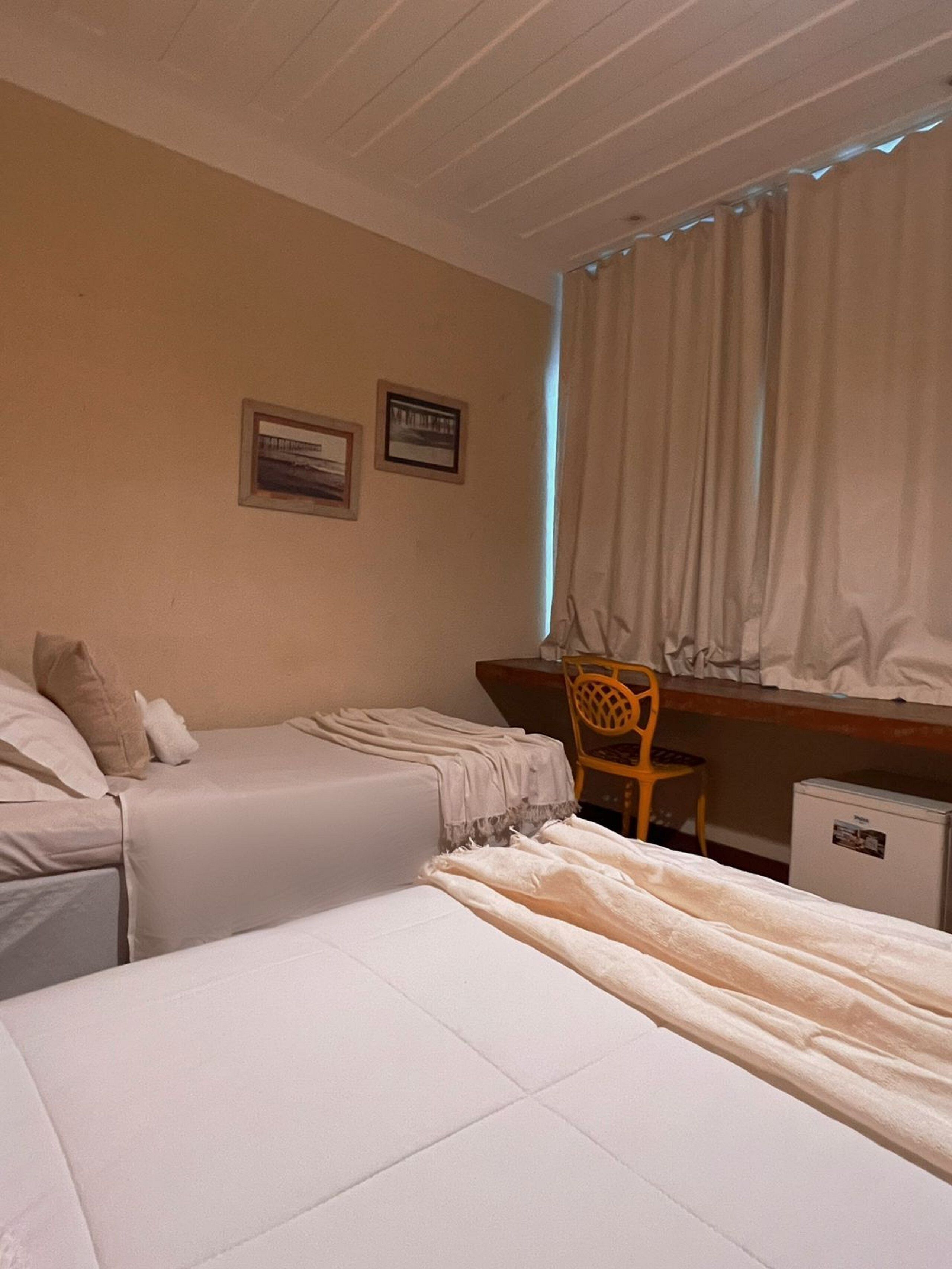 A bedroom with two beds, a desk, a chair, and a small refrigerator.