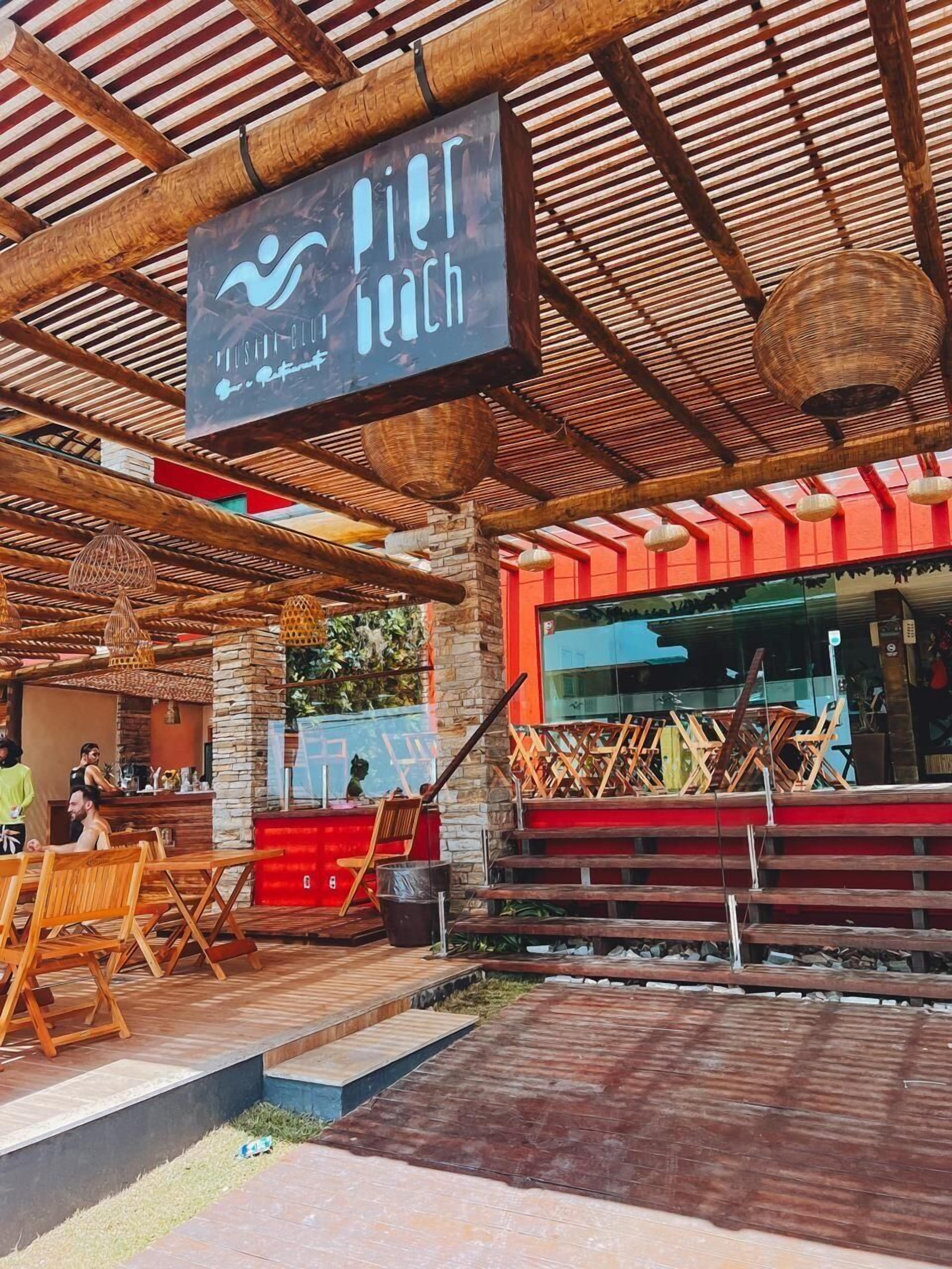An outdoor seating area with wooden chairs and tables, a sign for 'Pier Luich', and a red building in the background.