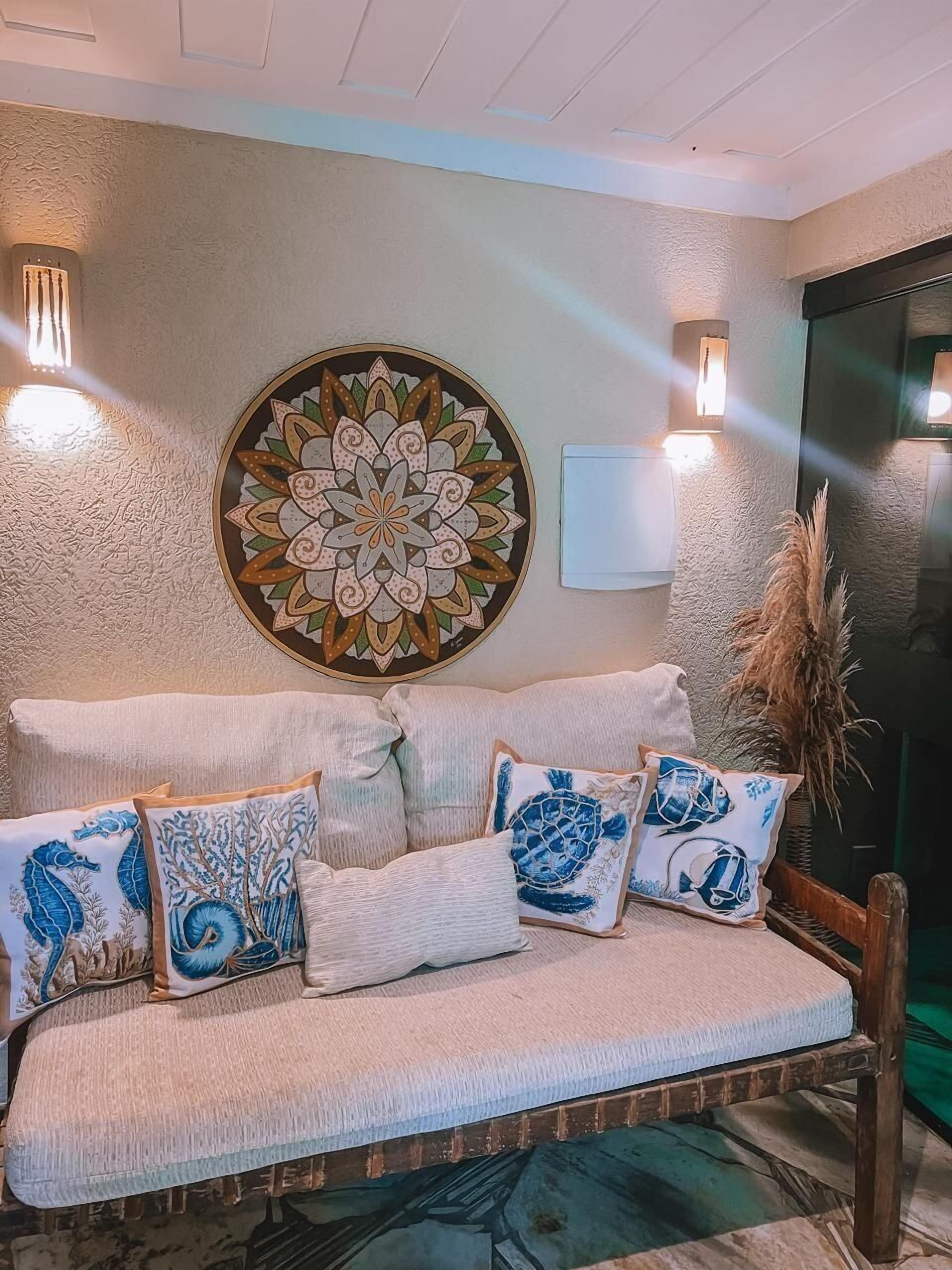 Un canapé beige agrémenté de coussins à motifs bleus et blancs, un élément décoratif mural et des lampes fixées au mur.