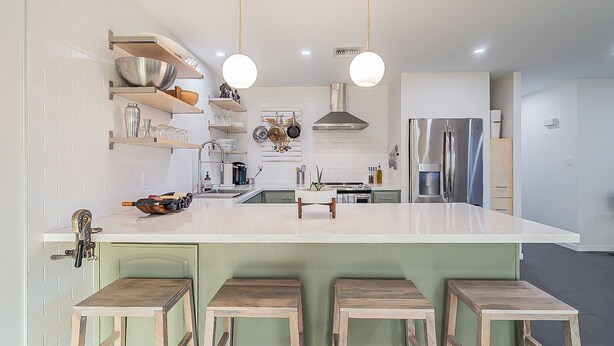 A modern kitchen with white subway tiles, stainless steel appliances, wooden stools, and pendant lighting. - Modern Oasis with Pool in the Valley of the Sun (Tempe)