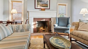 A living room with a fireplace, striped sofa, armchair, and a table with a decorative plate.
