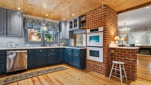A modern kitchen with dark blue cabinets, a brick accent wall, and built-in ovens.
