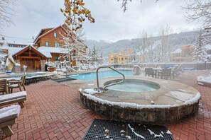 A hot tub surrounded by snow-covered furniture and a pool, with buildings in the background. - BBCS Black Bear Lodge Deluxe 2Bed 2Bath (Keystone)