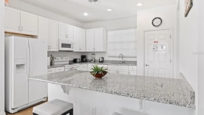 A modern kitchen with white cabinets, a granite countertop, and a small island with a plant. - Luxurious Villa - Near Disney - Golf Course (Davenport)