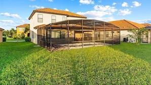 A house with a covered patio area, a lawn, and a neighboring building with a red-tiled roof. - Luxurious Villa - Near Disney - Golf Course (Davenport)