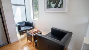 Una sala de estar moderna con un sofá de cuero negro, una mesa de centro de madera con un tablero de ajedrez y una planta enmarcada en la pared.