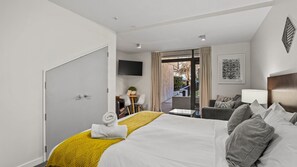 A hotel room with a bed, a desk, a chair, a TV, and a view of the outdoors. - The Alps Apartment - An alpine escape right in the city centre. (Queenstown)