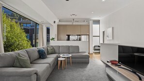 A modern living room with a sectional sofa, a small coffee table, and a flat-screen TV. - The Alps Apartment - An alpine escape right in the city centre. (Queenstown)