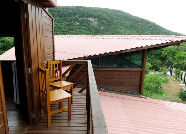 Una terraza de madera con una silla, una escalera y vistas a una ladera boscosa.