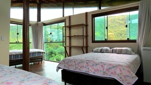 A bedroom with two beds, large windows, and a view of greenery. - Morada Fenix Hospedagem (Palhoça)