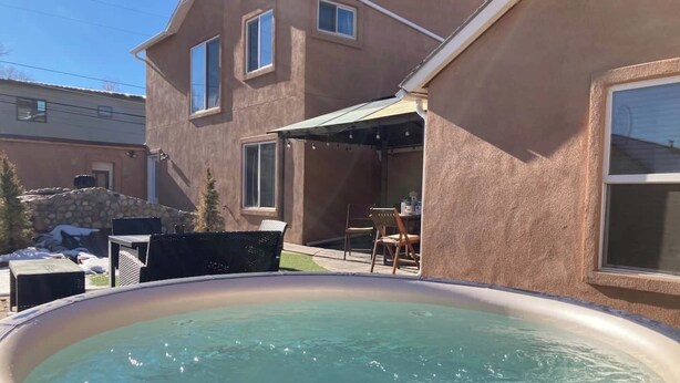 Un jacuzzi en un patio trasero, con un área de terraza, un muro de piedra y una casa al fondo.