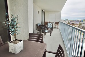 A balcony with a table and chairs, a potted plant, and a view of the beach and houses.