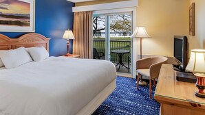 Une chambre d’hôtel avec un grand lit, un bureau avec une télévision, une chaise et un balcon offrant une vue sur le paysage.