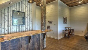 A rustic interior with a wooden bar counter, a wall-mounted sign, and a dining area with stools.