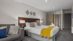A hotel room with a large bed, a sofa, a wardrobe, and a bathroom visible through an open door. - The Alps Studio - Cosy one bed right in the centre of Queenstown (Queenstown)