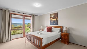 A bedroom with a bed, a nightstand, a lamp, a painting, and a view of the outdoors.