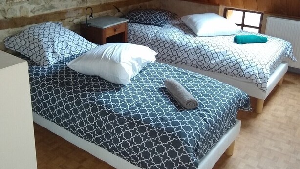 Una habitación con dos camas, cada una con ropa de cama y almohadas estampadas, una mesita de noche de madera y un ventanal que deja entrar luz natural.