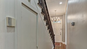 Un pasillo con suelo de madera, una puerta blanca al final, un candelabro y un termostato en la pared.