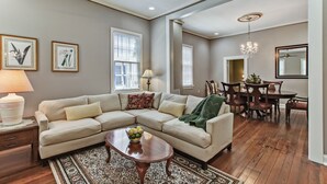 Una sala de estar con un sofá seccional color beige, una mesa de centro de madera, y un comedor con una mesa y sillas de madera.