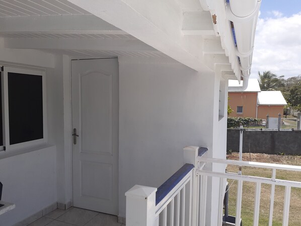 A white door with a window, a white railing, and a view of a building in the background.