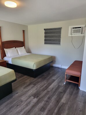 Una habitación con dos camas, un banco, una ventana con persianas y un equipo de aire acondicionado.