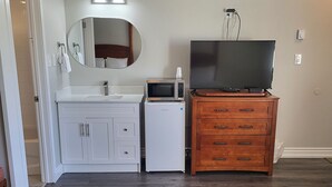 A room with a white vanity, a microwave, a television on a wooden dresser, and a mirror on the wall. - Studio 1 Motel (Cobourg)