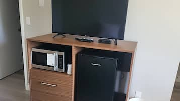 A compact living space with a flat-screen TV, a microwave, a mini-fridge, and a small trash bin.