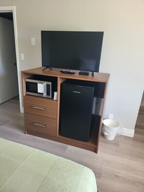 En kompakt opholdsstue med et fladskærms-tv, en mikroovn, et minikøleskab og en lille skraldespand.