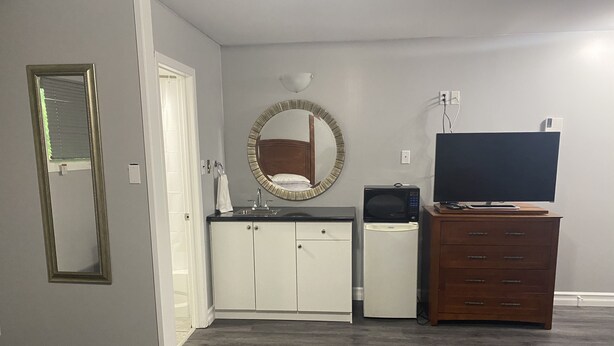 Een compacte leefruimte met een kitchenette, een houten dressoir, een televisie en een spiegel.