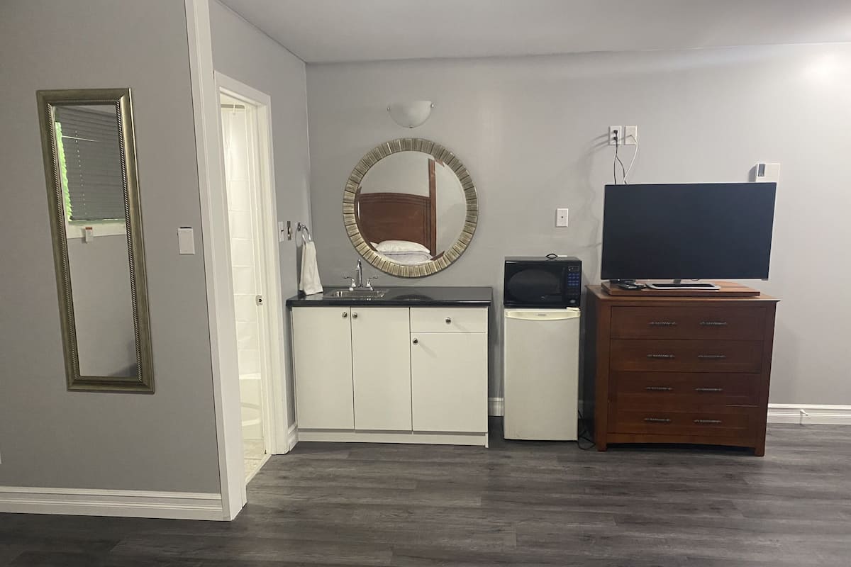 Un espacio habitable compacto con kitchenette, tocador de madera, televisor y espejo.