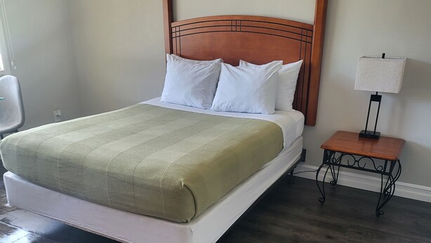 A neatly made bed with a wooden headboard, a bedside table with a lamp, and a chair. - Studio 1 Motel (Cobourg)