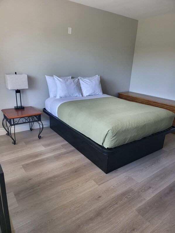 A bedroom with a bed, bedside table, lamp, and a wooden nightstand.