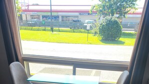A room with a window view of a parking lot and a building with signage. There is a table with two chairs and a red blanket on the floor. - Studio 1 Motel (Cobourg)
